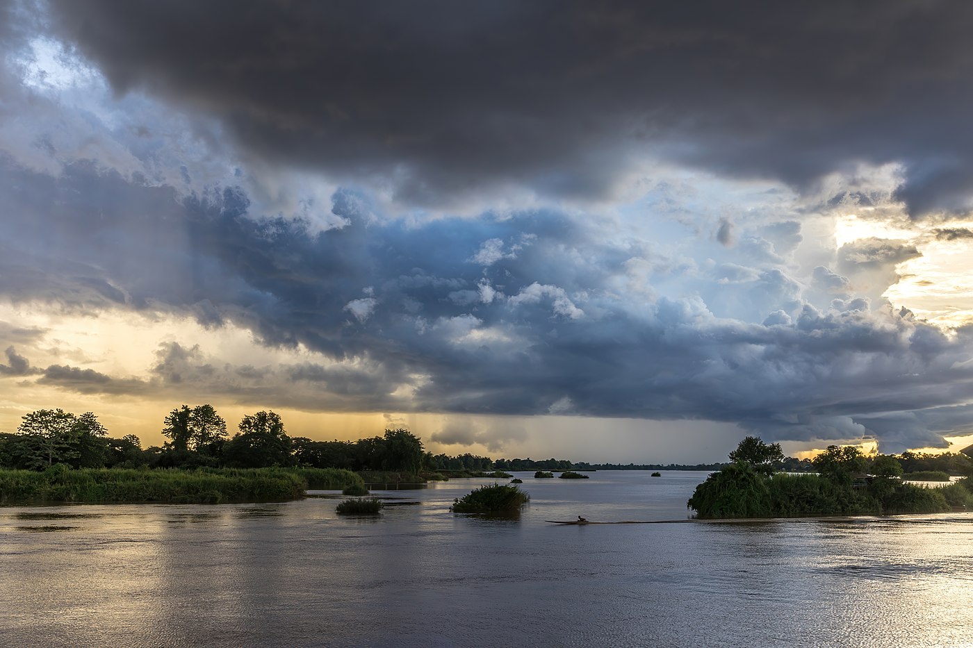 Blue and orange clouds over the Mekong with a pirogue running in the water at sunset in Don Det