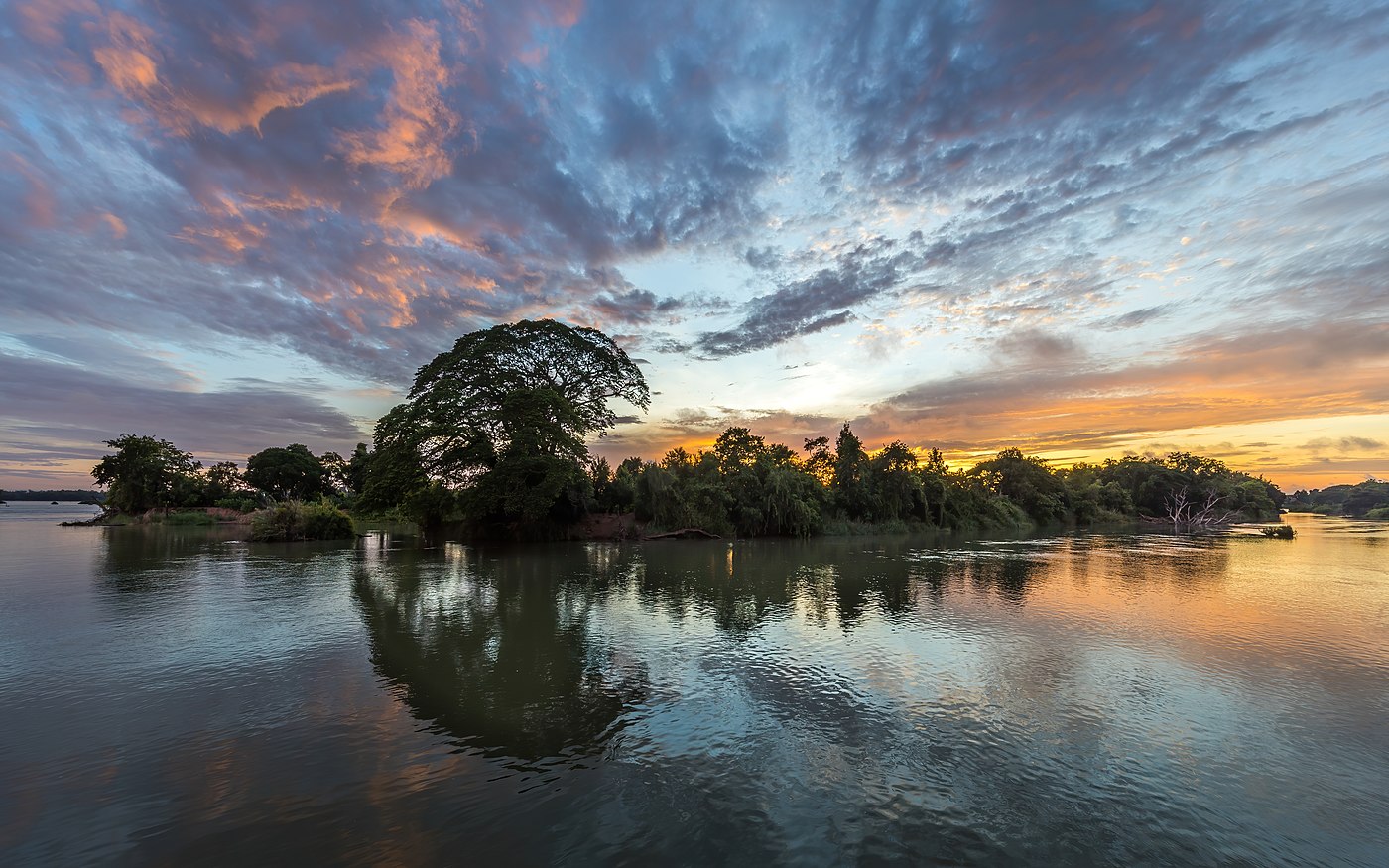 Colorful clouds and blue sky with water reflection of an island hosting a Samanea saman