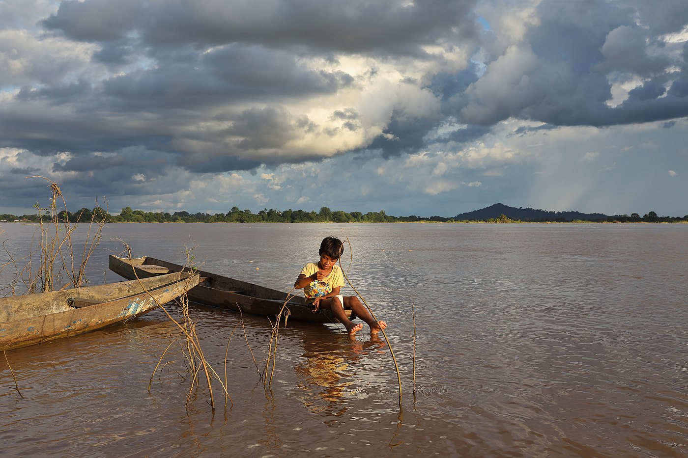 Jeune garçon assis sur son bateau, pêchant dans le Mékong