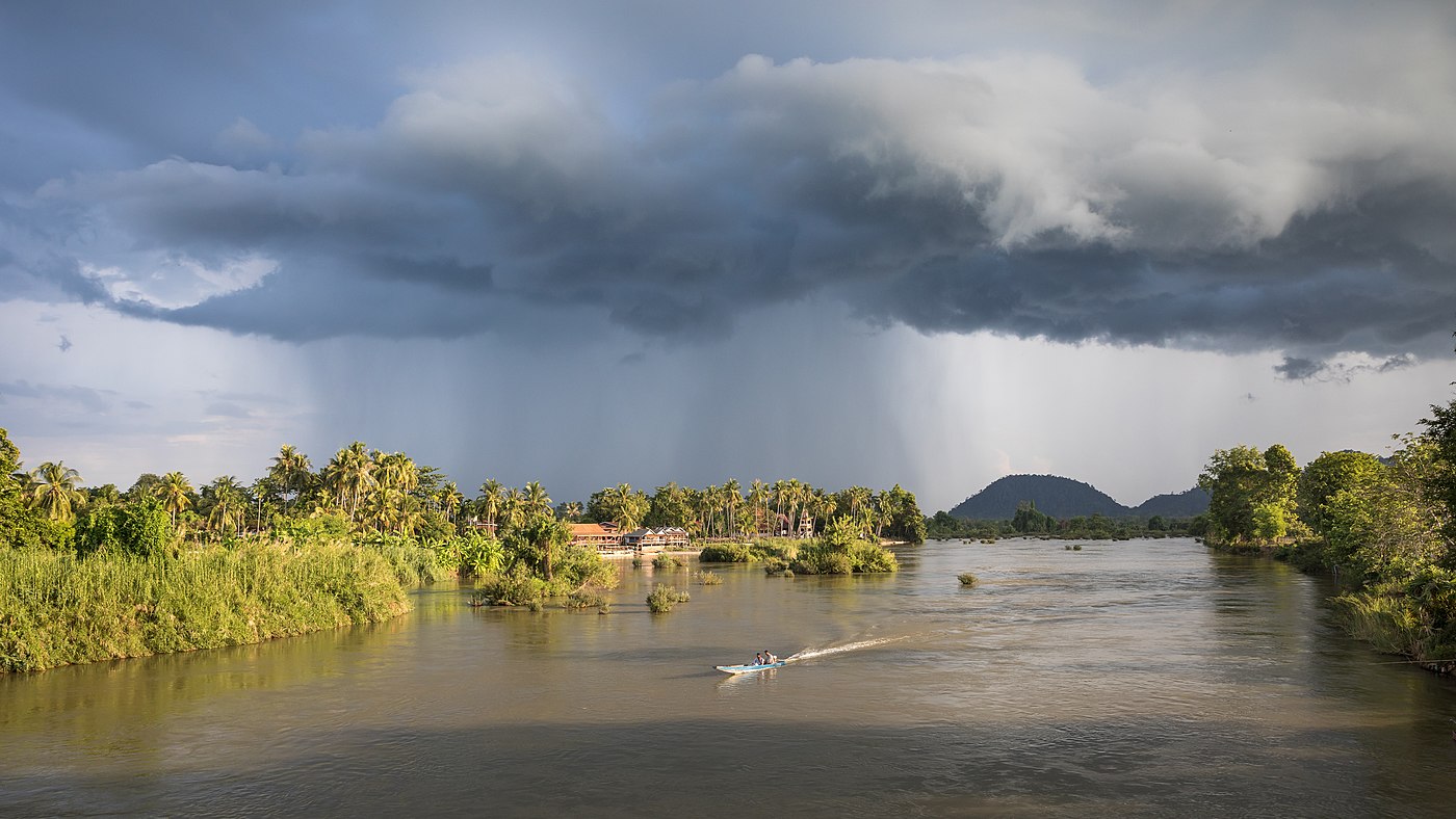 Landscape with stormy clouds and a pirogue on the Mekong at golden hour Don Det Laos