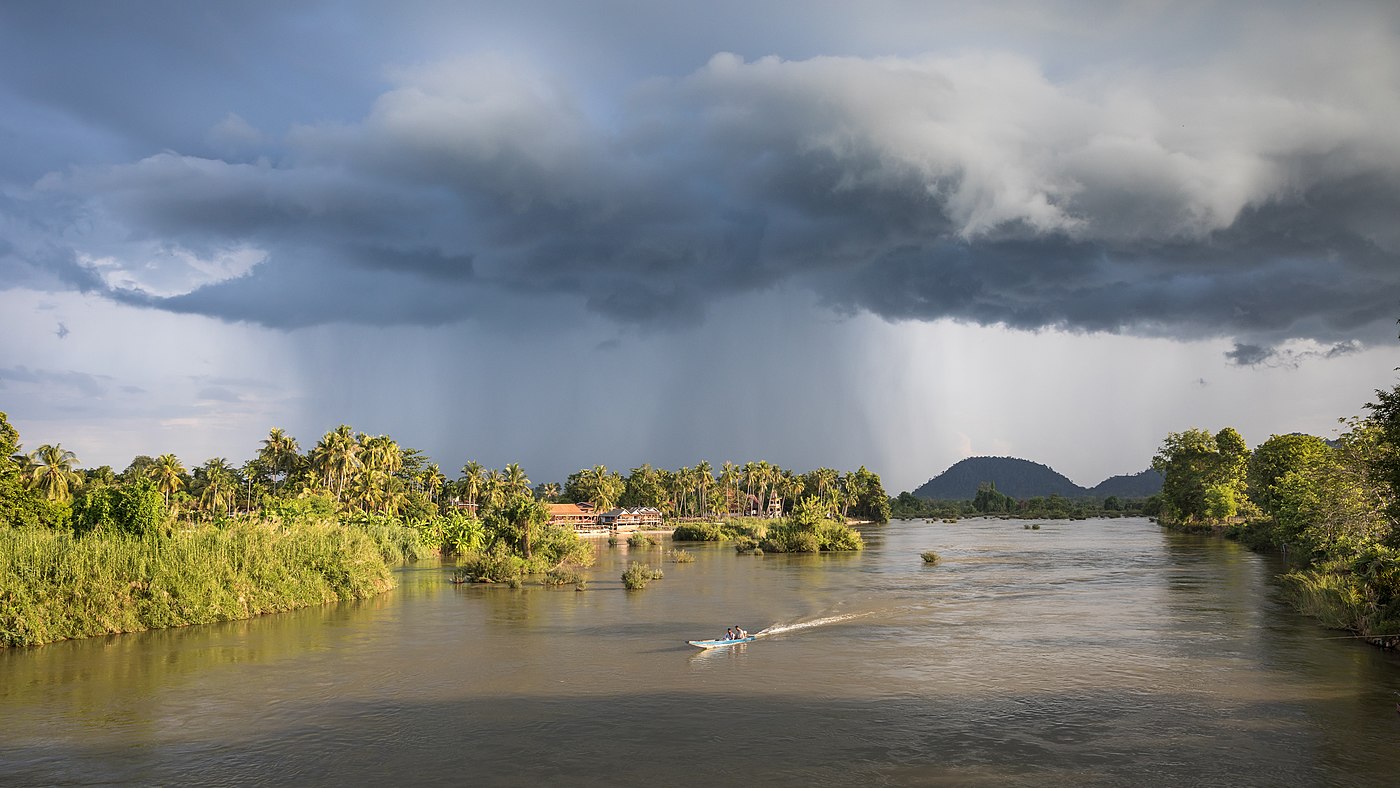 Paysage avec des nuages orageux et une pirogue sur le Mékong à l'heure dorée