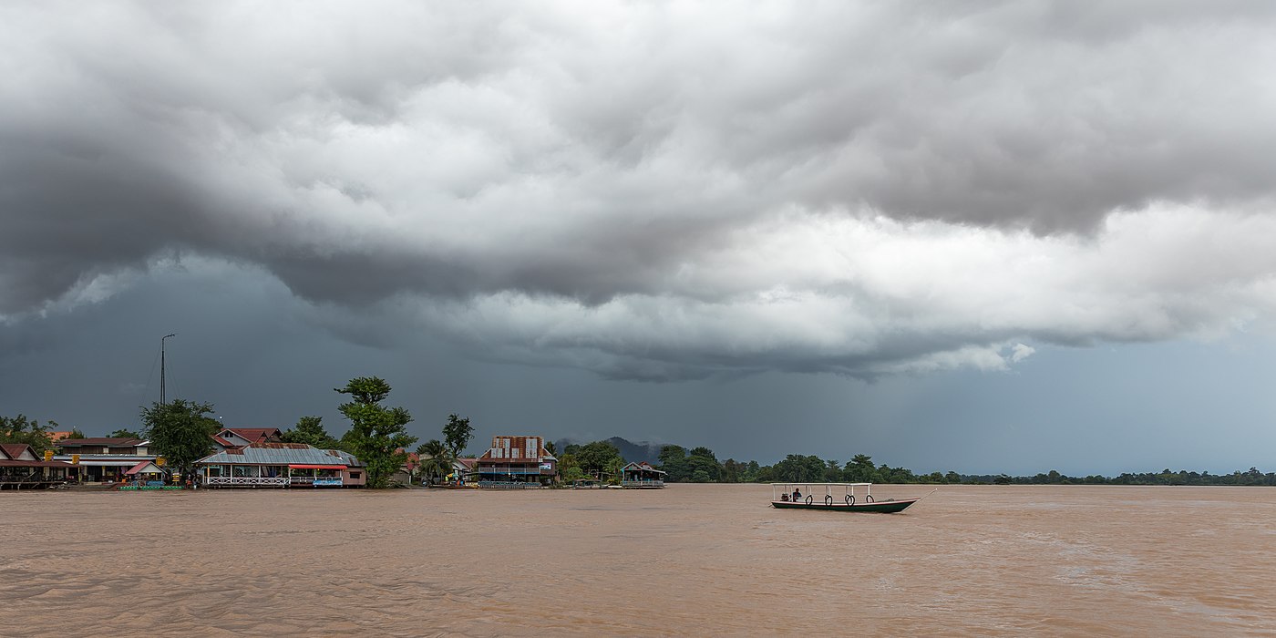 Pirogue on the Mekong river under heavy grey clouds during the monsoon before a storm