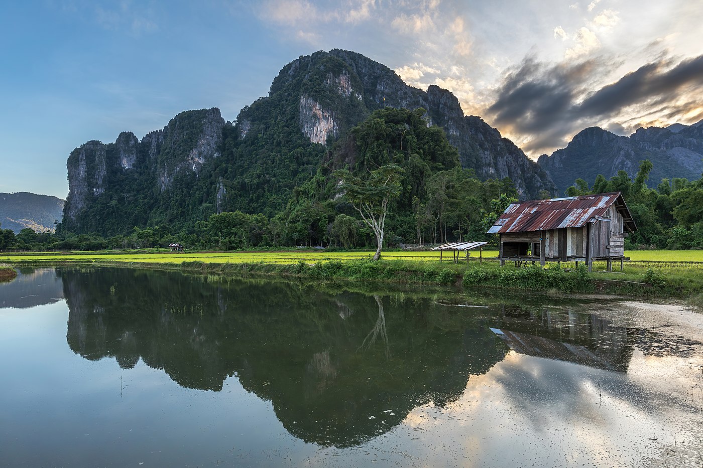 Water reflection of karst mountains, a wooden hut, trees and colorful clouds at sunset